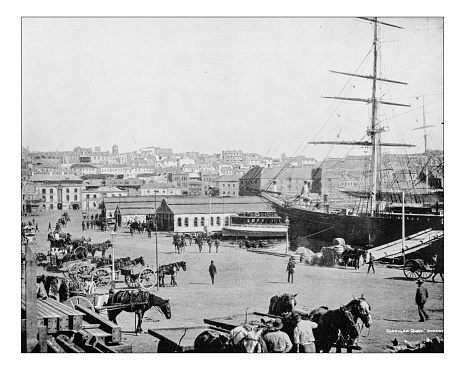 Antique photograph of the Circular Quay harbour (Sydney, New South Wales, Australia) in a late 19th century picture. The waterfront with the pedestrian area and the harbour buildings and docks.