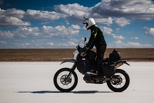 istock Man rides motorbike on salt pan under cloudy sky. 544126890