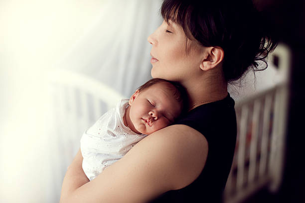 young Asian mother tenderly holds the sleeping on shoulder