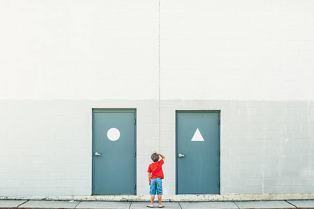 Gender confusion Small confused child scratching his head standing inbetween doors with gender signs, plenty of copyspace. unknown gender stock pictures, royalty-free photos & images