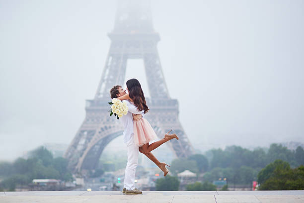 Romantic couple together in Paris Beautiful romantic couple in love with bunch of white roses having fun near the Eiffel tower in Paris on a cloudy and foggy rainy day paris france eiffel tower love kissing stock pictures, royalty-free photos & images