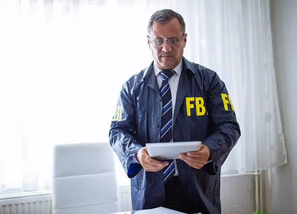 FBI agent, man working in the office on a crime. He is working on digital tablet.