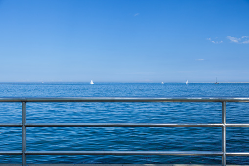 Bright daylight image of sailboats in Lake Michigan from coast with metal railing