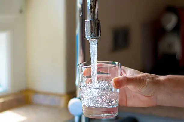 Woman filling a glass of water from a stainless steel or chrome tap or faucet, close up on her hand and the glass with running water and air bubbles