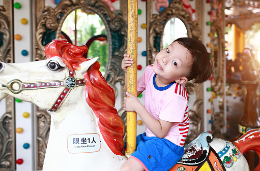 Child having fun riding on a colorful carnival carousel 