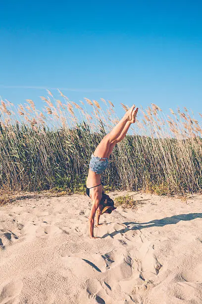 Photo of Young hipster woman outdoor doing hand stand on the beach