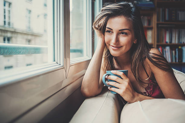 Happy and comfortable at home in the morning Beautiful young woman holding a cup of coffee looking through a house window. Shot made during Istockalypse Paris 2016 event. natural beauty people stock pictures, royalty-free photos & images