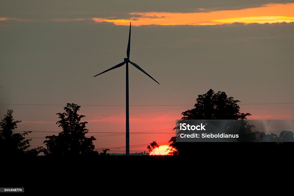 Sun setting down behind Wind turbine and electricity lines. Back Lit Stock Photo