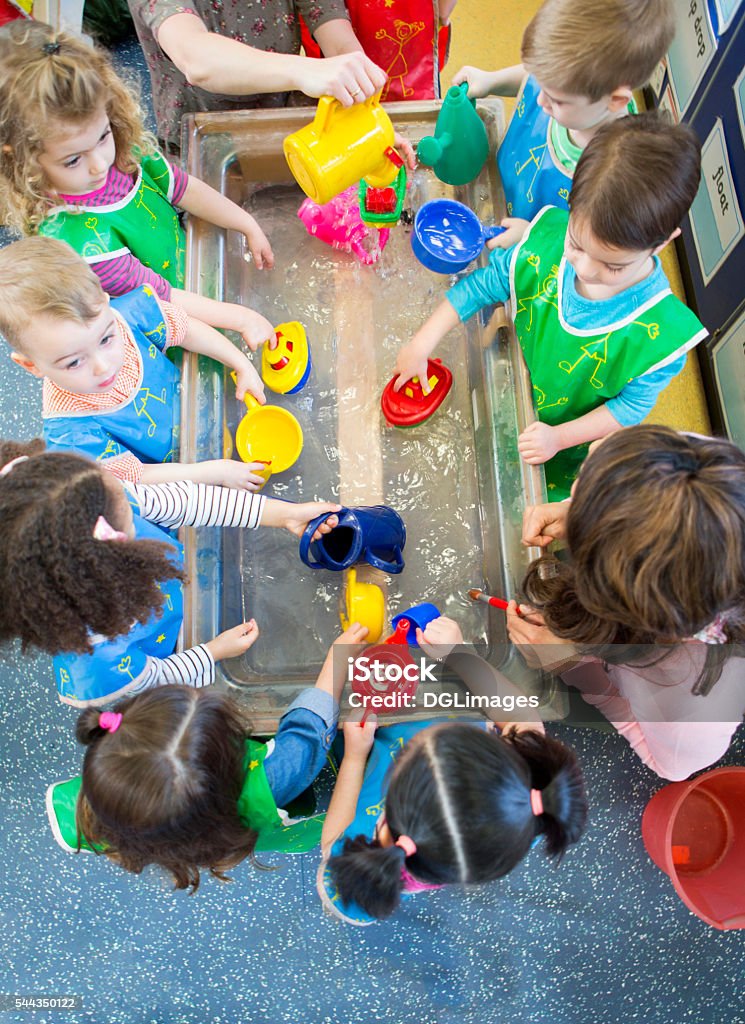 Aqua Play at Nursery Overhead view of a class of nursery children playing at a water table. They are all wearing aprons and using plastic toys. Preschool Stock Photo