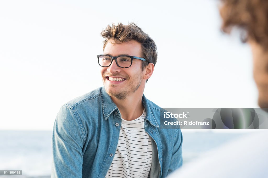 Carefree man Handsome man smiling at the beach and looking away. Portrait of a cheerful guy enjoying summer vacation. Handsome man with eyeglasses in casual relaxing outdoor with friend. Men Stock Photo