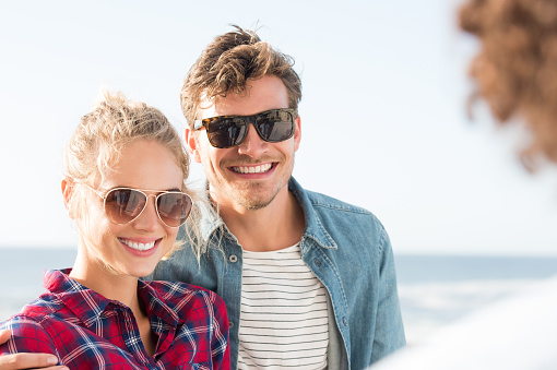 Happy girlfriend and boyfriend having fun and wearing sunglasses during sunset. Portrait of happy couple posing for a picture. Smiling young couple enjoying with their friend.