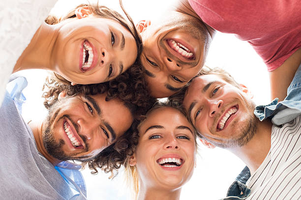 Happy friends embracing Directly below shot of young friends forming huddle. Low angle view of girls and guys with their head forming a circle. Portrait of young people looking at camera. Friendship and unity concept. teeth bonding stock pictures, royalty-free photos & images