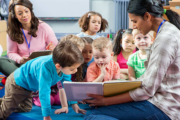 Storytime at Nursery Female teacher giving a lesson to nursery students. They are sitting on the floor and there is a teacher taking notes. preschool age photos stock pictures, royalty-free photos & images