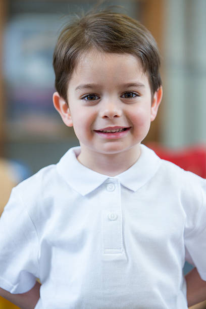 Portrait of a school boy. He is wearing a white shirt and smiling for the camera.