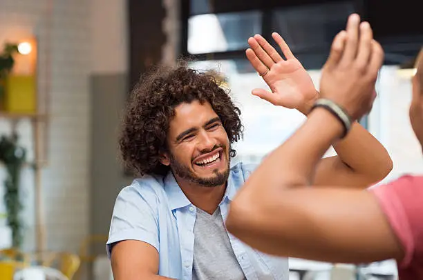 Portrait of friends giving high five at cafe while having lunch. Young guys friends giving a high five, slapping each others hand in congratulations while sitting in cafeteria.