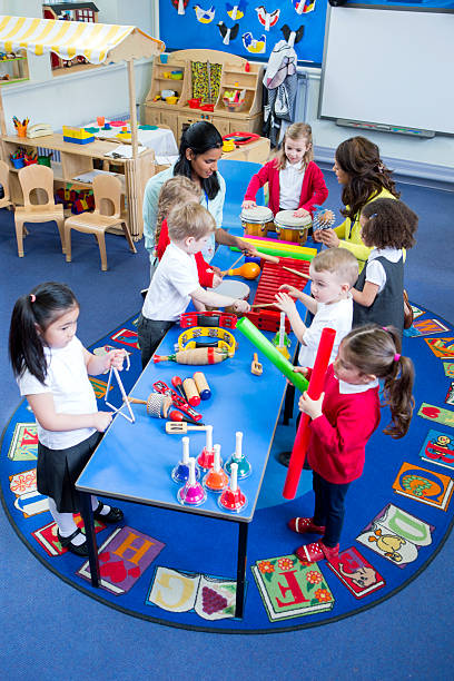 Noisy Nursery Lesson Nursery children playing with musical instruments in their music lesson with teachers. They are in the classroom. teacher classroom child education stock pictures, royalty-free photos & images