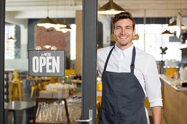 New small business Portrait of smiling owner standing at his restaurant gate with open signboard. Young entrepreneur leaning at the cafeteria door and looking at camera. Chef or waiter standing in front of coffee shop. cafeteria worker photos stock pictures, royalty-free photos & images