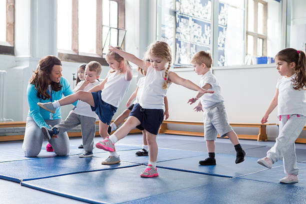 Just a little higher! Nursery teacher helping one of her students during a physical education lesson. preschool building photos stock pictures, royalty-free photos & images
