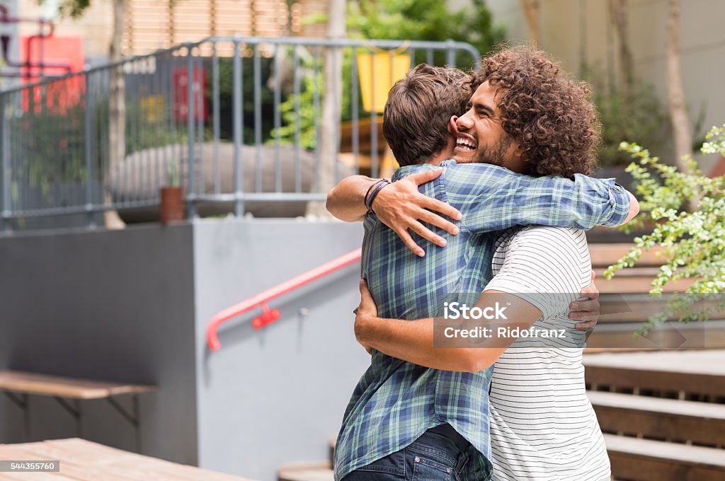 Friends embracing each other Cheerful best friends embracing each other outside coffee shop. Two young multiethnic guys hugging each other. Happy smiling best friends meeting each other after a long time with a hug. Embracing Stock Photo