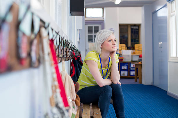 Stressed School Teacher Young, female teacher sitting on a bench in the cloakroom of school. She is looking pensively out of the window. preschool building stock pictures, royalty-free photos & images