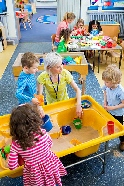 Creative Nursery Lesson Elevated view of teachers doing activities with children in nursery. Some are playing in a sand box and the others are making crafts. sandbox photos stock pictures, royalty-free photos & images