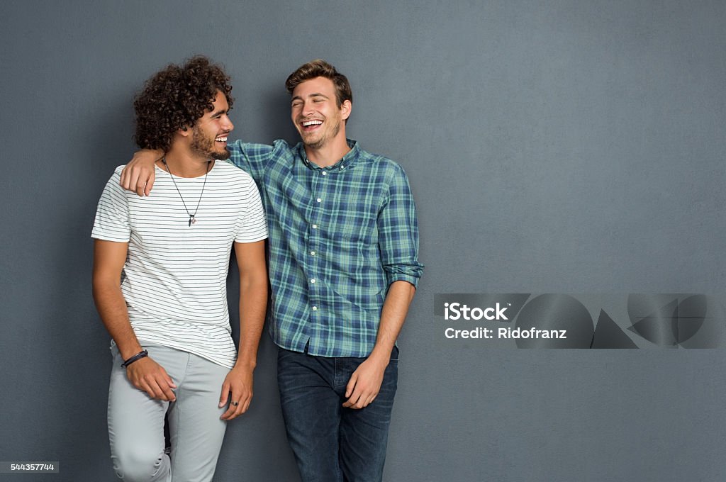 Friends laughing and enjoying Two friends in casual wear standing and laughing together. Best friends enjoying isolated over grey background. Two men having fun isolated over grey wall with copy space. Friendship Stock Photo