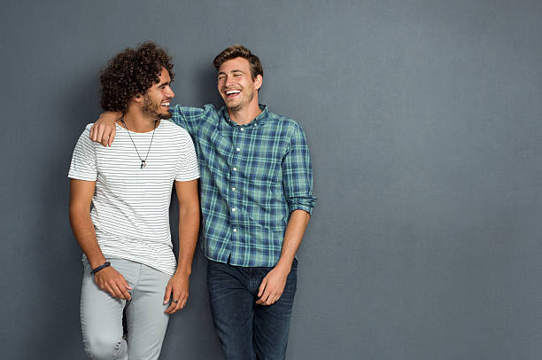 Friends laughing and enjoying Two friends in casual wear standing and laughing together. Best friends enjoying isolated over grey background. Two men having fun isolated over grey wall with copy space. arm around stock pictures, royalty-free photos & images