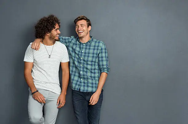 Two friends in casual wear standing and laughing together. Best friends enjoying isolated over grey background. Two men having fun isolated over grey wall with copy space.