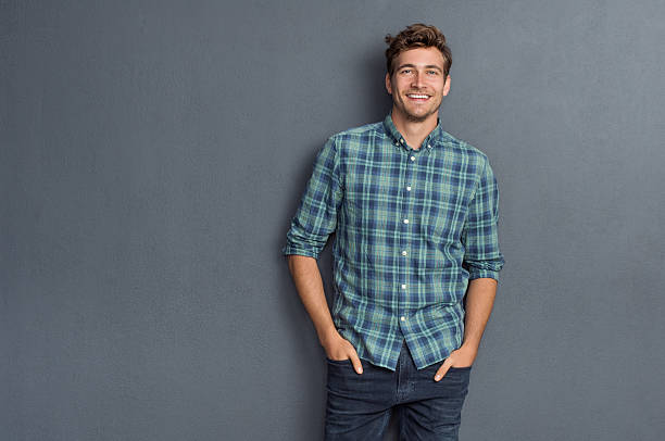 Pride man smiling Handsome young man on grey background looking at camera. Portrait of laughing young man with hands in pockets leaning against grey wall. Happy guy smiling. leaning photos stock pictures, royalty-free photos & images