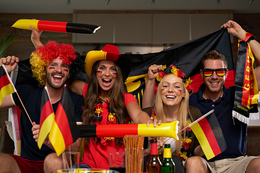 four happy German friends watching tv at home cheering for Germany