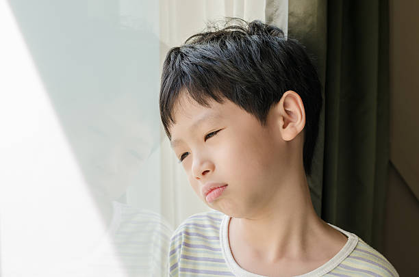 Sad boy looking out of window stock photo
