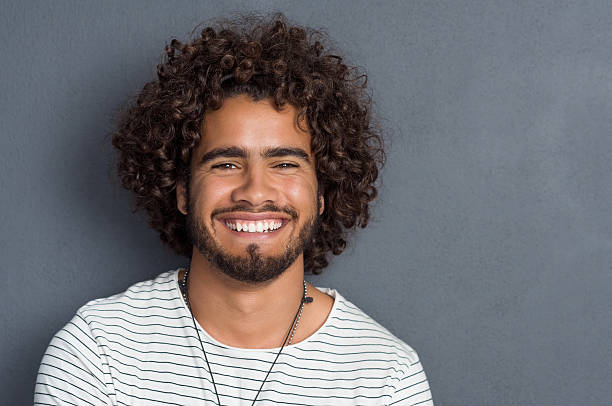 Happy friendly guy Portrait of a happy cheerful young man looking at camera. Handsome young man with beard and curly hair standing against grey background. Close up face of multi ethnic young man isolated against grey wall. curly stock pictures, royalty-free photos & images