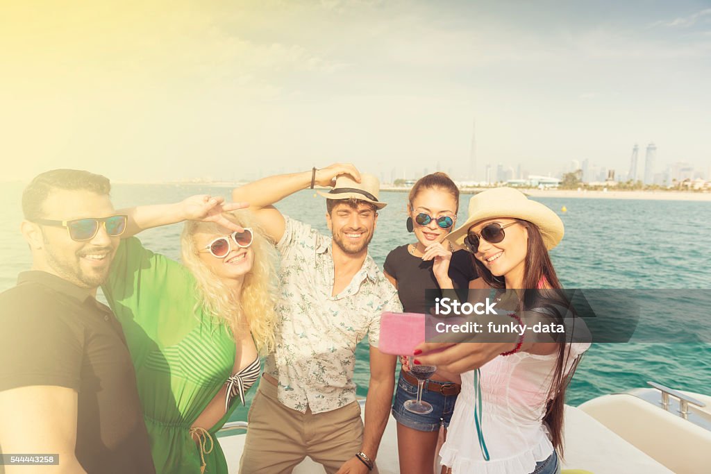 Friends having boat party in Dubai A group of multicultural friends are taking a selfie during a boat party on Dubai shores at the Emirates. Dubai Stock Photo