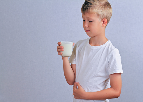 Lactose intolerance. Dairy Intolerant Child with stomach pain holding a glass of milk.
