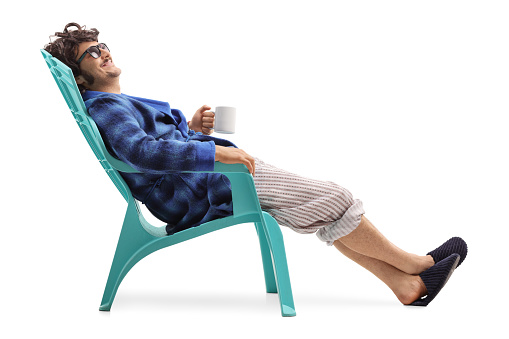 Relaxed man sitting on a blue plastic chair and holding a cup of coffee isolated on white background