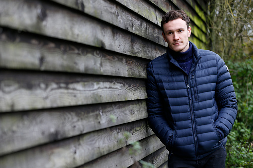 Outdoor Portrait Of Man Leaning Against Wooden Building