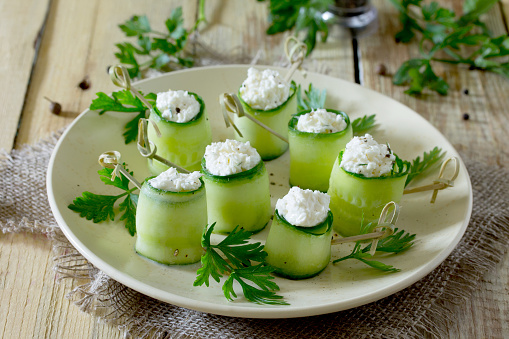 Cucumber rolls stuffed with feta cheese, dill and olives on a wooden table.