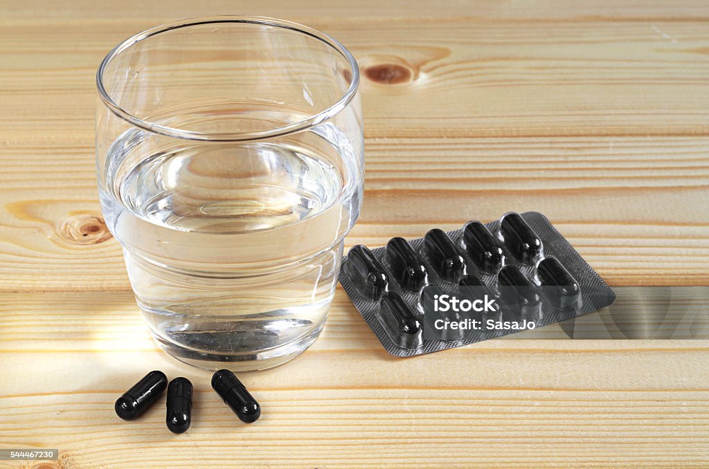 Activated charcoal and water Medical capsules with activated charcoal and glass of water on wooden table Coal Stock Photo