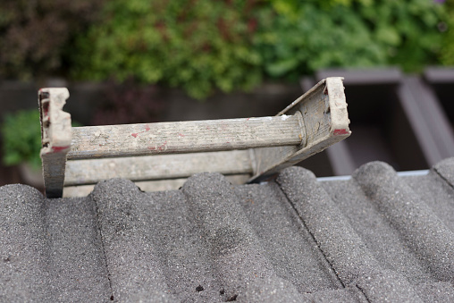 selective focus on grey, old metal ladder seen from roof top with tiles.