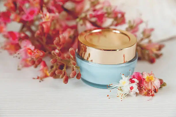 There White and Pink  Branches of Chestnut Tree with Blue and Golden Jar of Cream are on White Table,Selective Focus