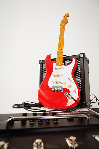 Cape Town, South Africa- July 2, 2016:  A Stratocaster in the vintage Fender color Fiesta Red. This instrument is part of the Classic Vibe series manufactured in China by the Fender subsidiary Squier in 2013. The Classic Vibe guitars have been acclaimed by reviewers and guitarists around the world for their superior quality at comparatively affordable prices, although they are more expensive than other Squiers. This model reproduces vintage features of Fender Strats made in the 1950s. It is propped against a Roland Cube 80X amp with a defocussed multi-effects unit in the foreground.