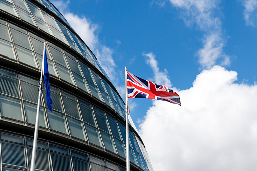The European Union (EU) flag and waving British Union flag at City Hall against blue sky.