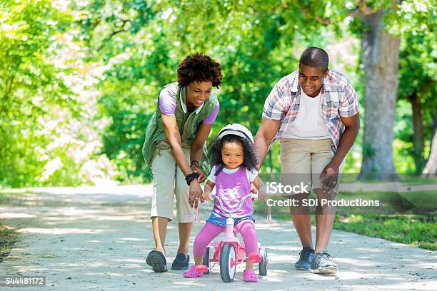 Happy Mother And Father Teaching Toddler Daughter To Ride Tricycle Stock Photo - Download Image Now