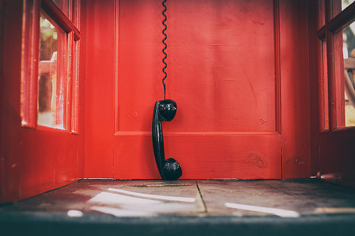 telephone receiver hanging touching the floor in a red call telephone booth. the concept of technological progress and the development of communication. Hanging up