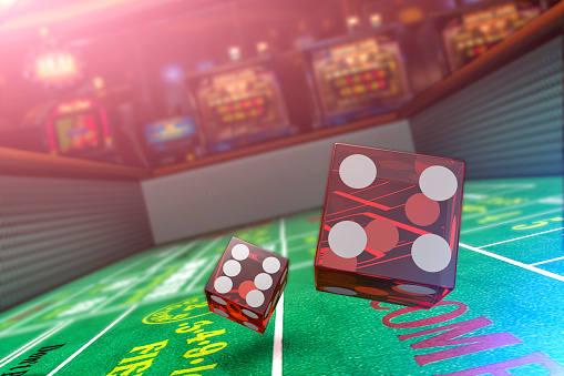 A close up view of dice being rolled on a craps table in a casino with slot machines in the background.  Please see my portfolio for other gambling related images. 