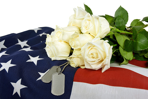 Military dog tags and white rose bouquet on American flag.