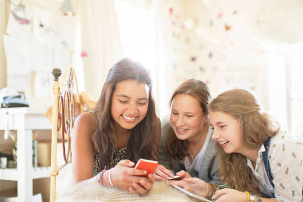 istock Three teenage girls using smartphone together while lying on bed in bedroom 544488685