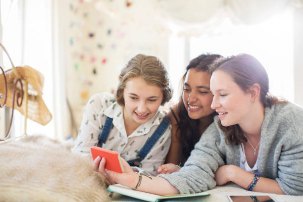 istock Three teenage girls using smartphone together while lying on bed 544488877