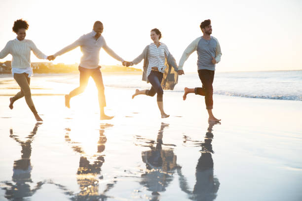 istock Group of four friends holding hands and running on beach 544489241