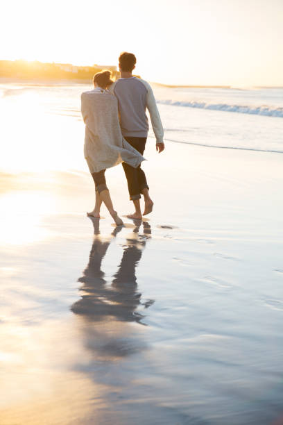 istock Young couple holding hands and walking on beach at sunset 544489535